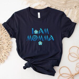 Pode incluir: Camiseta azul marinho com o texto "I AM MOMMA" em uma fonte azul e branca com um gr&aacute;fico de flor azul.