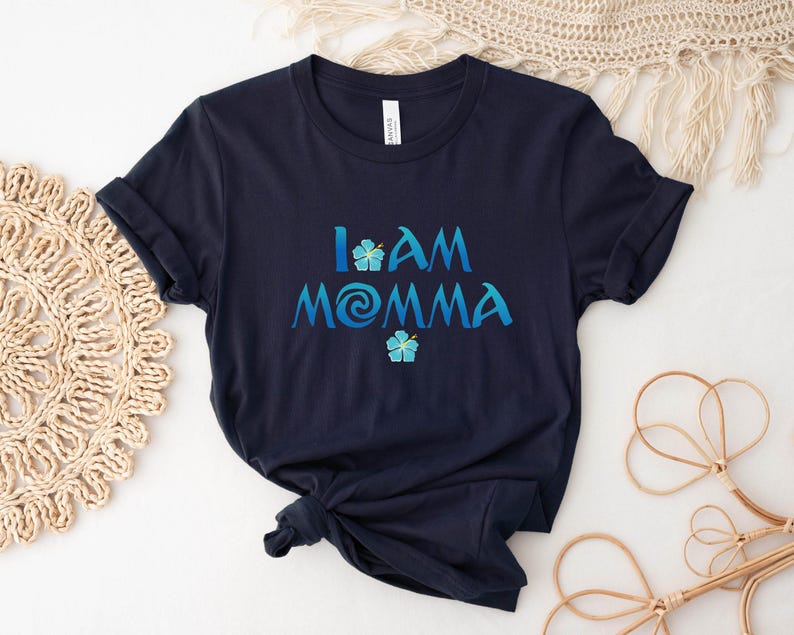 Pode incluir: Camiseta azul marinho com o texto "I AM MOMMA" em uma fonte azul e branca com um gr&aacute;fico de flor azul.