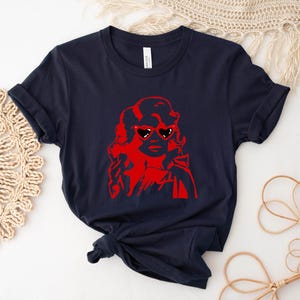 May include: A navy blue t-shirt with a red graphic of a woman wearing heart-shaped sunglasses.