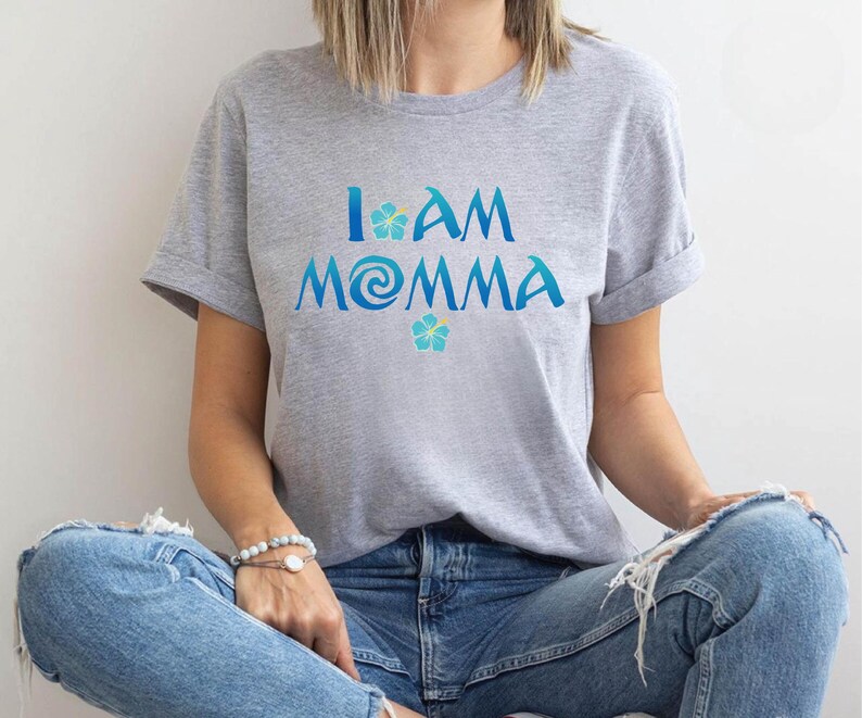 Pode incluir: Uma camiseta cinza com o texto "I am Momma" em azul e amarelo. O texto &eacute; estilizado com um redemoinho azul e uma flor amarela.