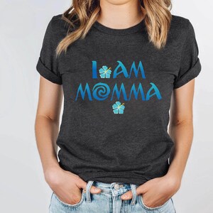 Pode incluir: Uma camiseta cinza escura com o texto "I AM MOMMA" em azul com um redemoinho azul e desenhos de flores azuis.