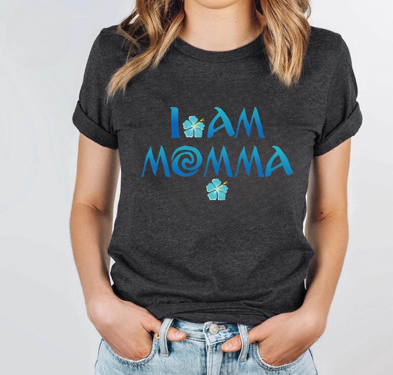 Pode incluir: Uma camiseta cinza escura com o texto "I AM MOMMA" em azul com um redemoinho azul e desenhos de flores azuis.