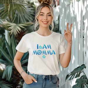 Pode incluir: Camiseta branca com um gr&aacute;fico azul e verde que diz "I am Momma" com um design de flores.