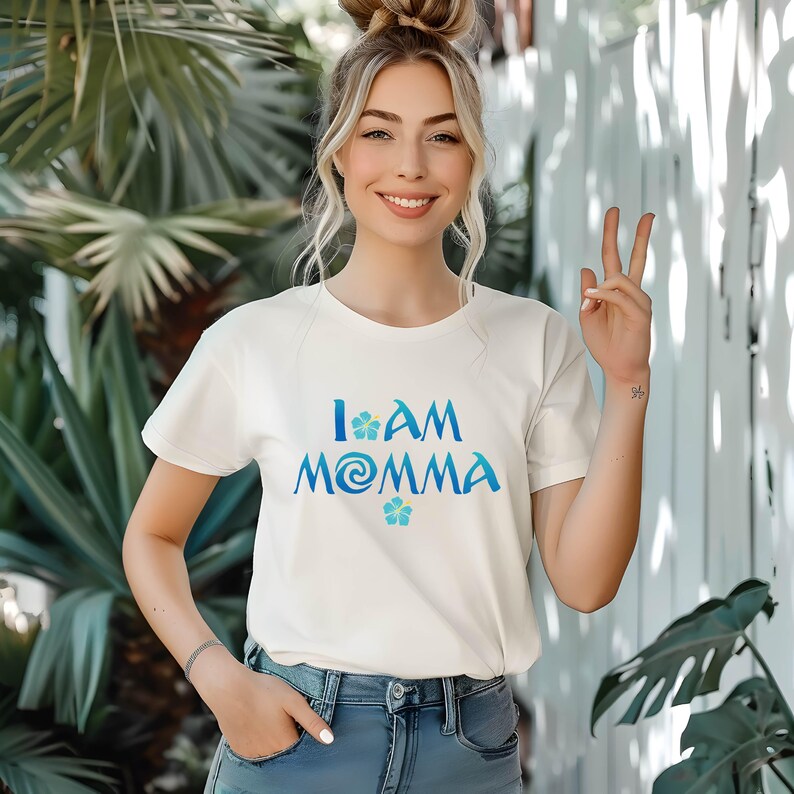 Pode incluir: Camiseta branca com um gr&aacute;fico azul e verde que diz "I am Momma" com um design de flores.