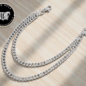 May include: Silver-colored wallet chain with two lobster claw clasps. The chain is made of curb links. A circular logo with the word "GOTHIC" in a stylized font is visible.