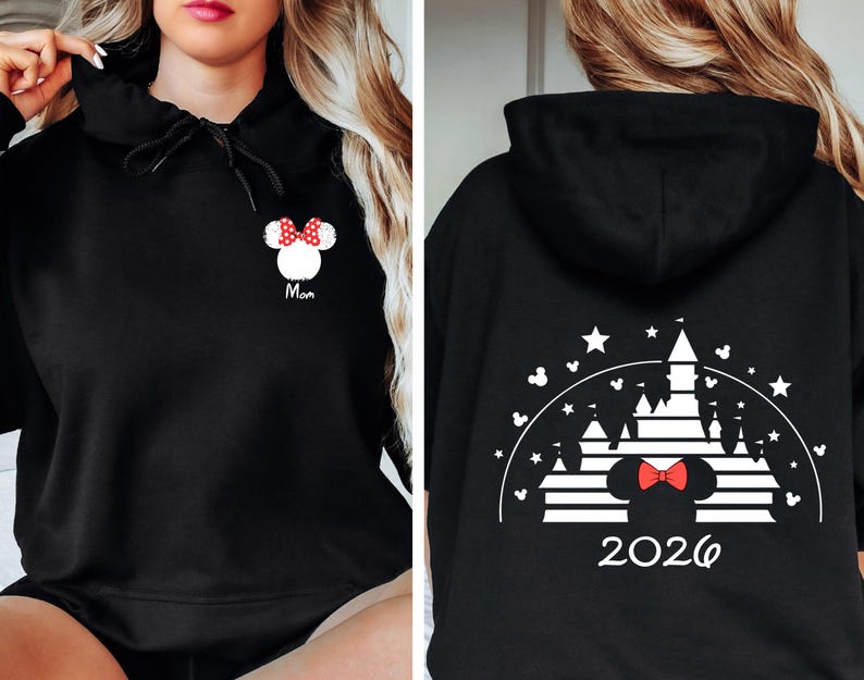 Puede incluir: Sudadera con capucha negra con dise&ntilde;o de Minnie Mouse. La parte delantera muestra una cabeza de Minnie Mouse con un lazo rojo y la palabra "Mom". La parte trasera presenta una silueta de castillo, estrellas y el a&ntilde;o "2026".