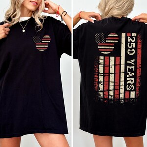 May include: Black t-shirt with a patriotic design. The front shows a Mickey Mouse-shaped design with the American flag. The back features a larger flag design with the text "250 YEARS".