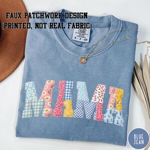 May include: A light blue t-shirt with the word "MAMA" in a patchwork design. The letters are made of various floral and gingham patterns. The shirt also has the text "FAUX PATCHWORK DESIGN (PRINTED, NOT REAL FABRIC)" and a small gold necklace.