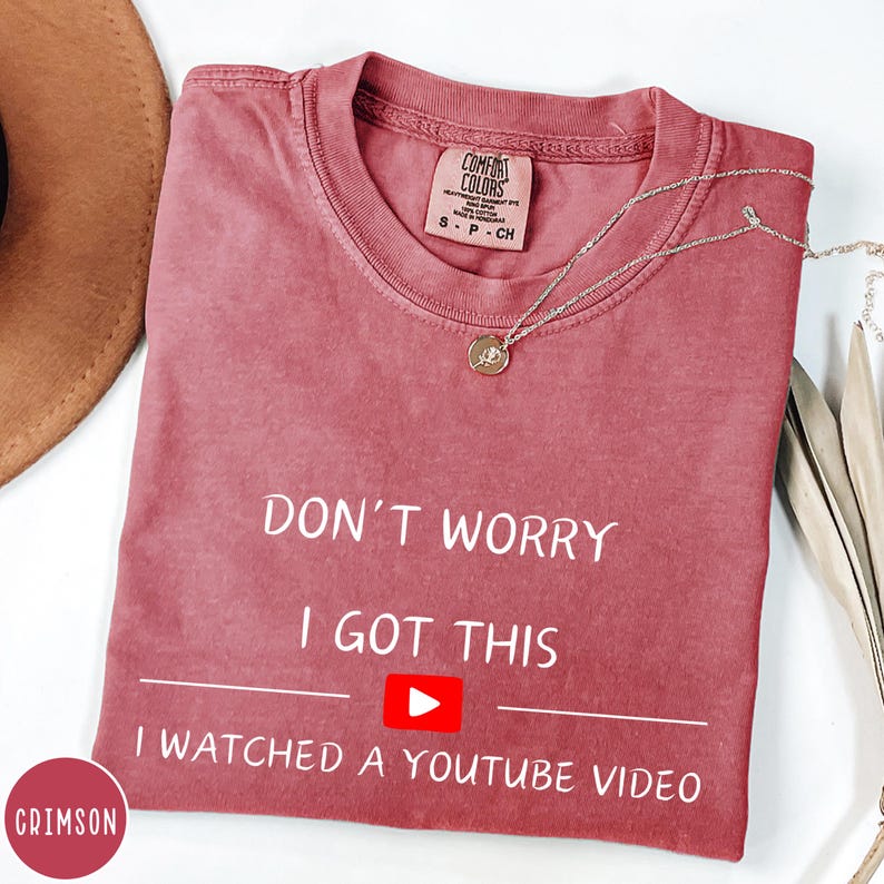 May include: Crimson-colored t-shirt with the text "DON'T WORRY I GOT THIS I WATCHED A YOUTUBE VIDEO". The shirt has a crew neck and a small tag that says "COMFORT COLORS". A silver necklace with a round pendant is on the shirt.