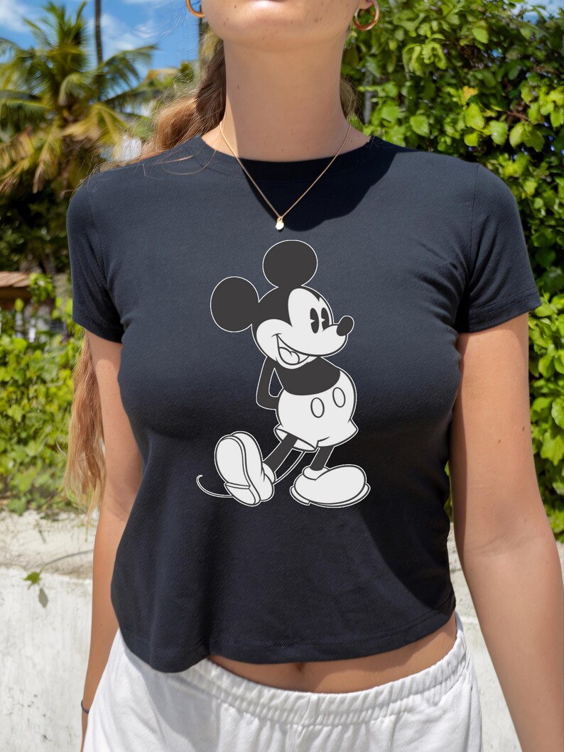 May include: Black crop top featuring a classic Mickey Mouse graphic in black and white. The cartoon character is depicted in a side pose with a cheerful expression. The top has short sleeves and a round neckline, perfect for casual wear.