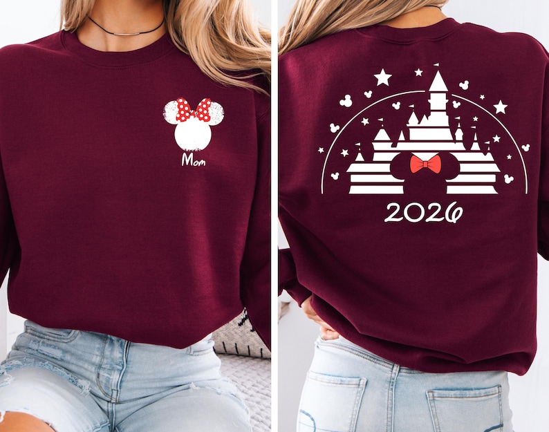Puede incluir: Sudadera burdeos con un dise&ntilde;o de Minnie Mouse blanco y un lazo rojo, con la palabra "Mom". La parte trasera presenta un dise&ntilde;o de castillo blanco, un lazo de Minnie Mouse y el a&ntilde;o "2026".