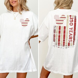 May include: White t-shirt with a Mickey Mouse-themed design in red and beige. The front has a small graphic, and the back features a larger design with the text "250 YEARS".