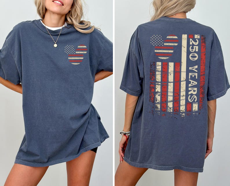 May include: A navy blue t-shirt with a distressed American flag design. The front features a Mickey Mouse head shape with the flag's stars and stripes. The back displays a larger flag design with the text "250 YEARS".