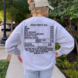 May include: Gray sweatshirt with a receipt-style graphic that reads "Jesus Paid It All" with a list of sins and the price paid for each. The text at the bottom reads "For the wages of sin is death, but the gift of God is eternal life in Christ Jesus our Lord. Romans 6.23"