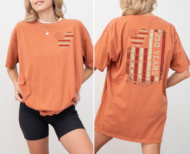 May include: Burnt orange t-shirt with a graphic design on the front and back. The front features two circles with a dotted and striped pattern. The back displays a distressed American flag design with the text "250 YEARS".
