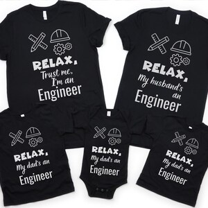 May include: Set of four black t-shirts with white text and graphics. The shirts feature the text "Relax, Trust me, I'm an Engineer", "Relax, My husband's an Engineer", "Relax, My dad's an Engineer", and "Relax, My dad's an Engineer".