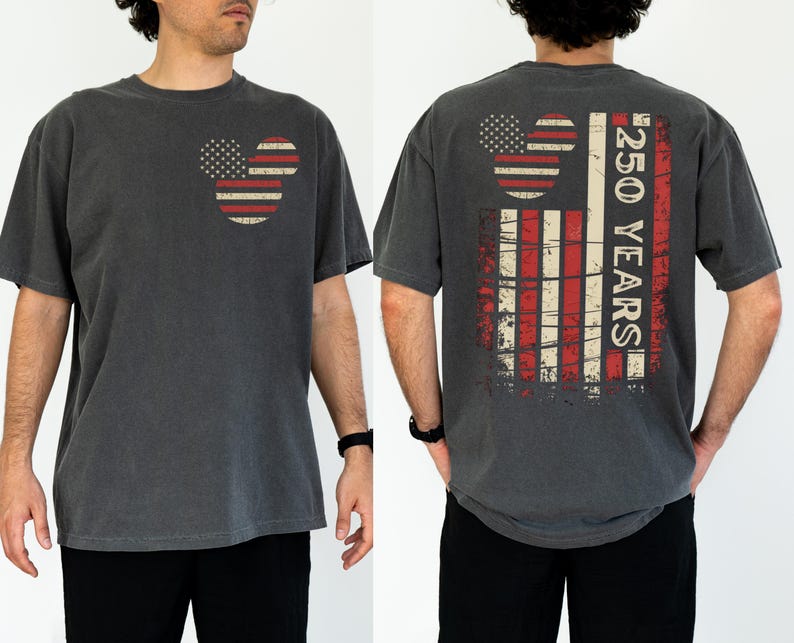 May include: Dark grey t-shirt with a distressed American flag design in the shape of Mickey Mouse ears on the front. The back of the shirt features a larger flag design and the text "250 YEARS".