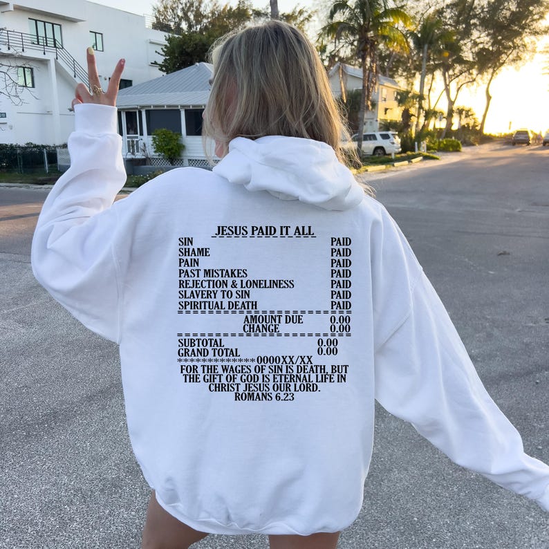 May include: White hoodie with a receipt-style graphic on the back. The graphic says "Jesus Paid It All" and lists various sins with the word "Paid" next to each. The graphic also includes a receipt total of 0.00 and a quote from Romans 6:23.