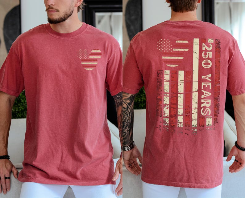 May include: A red t-shirt with a heart-shaped American flag on the front. The back shows a distressed American flag graphic and the text "250 YEARS". The shirt has a vintage appearance. The design is patriotic and commemorates an anniversary.