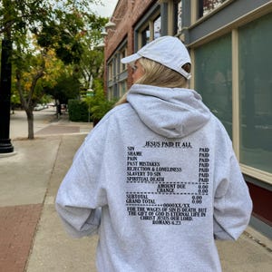 May include: Gray hooded sweatshirt with the text "JESUS PAID IT ALL" and a list of sins and the word "PAID" next to each. The text also includes "AMOUNT DUE 0.00", "CHANGE 0.00", "SUBTOTAL 0.00", "GRAND TOTAL 0.00", "FOR THE WAGES OF SIN IS DEATH, BUT THE GIFT OF GOD IS ETERNAL LIFE IN CHRIST JESUS OUR LORD. ROMANS 6.23".