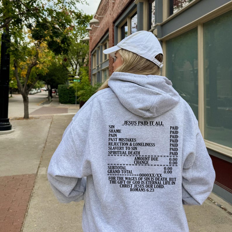 May include: Gray hooded sweatshirt with the text "JESUS PAID IT ALL" and a list of sins and the word "PAID" next to each. The text also includes "AMOUNT DUE 0.00", "CHANGE 0.00", "SUBTOTAL 0.00", "GRAND TOTAL 0.00", "FOR THE WAGES OF SIN IS DEATH, BUT THE GIFT OF GOD IS ETERNAL LIFE IN CHRIST JESUS OUR LORD. ROMANS 6.23".