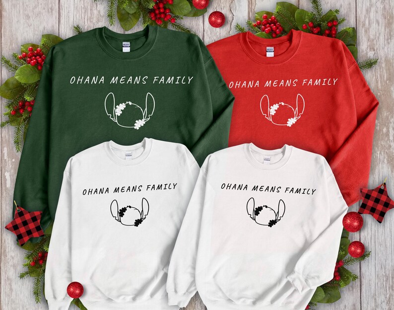 May include: Four sweatshirts in green, red, and white, each with the text "OHANA MEANS FAMILY" and a cartoon character outline. Festive holiday decorations surround the shirts, including red baubles and greenery.