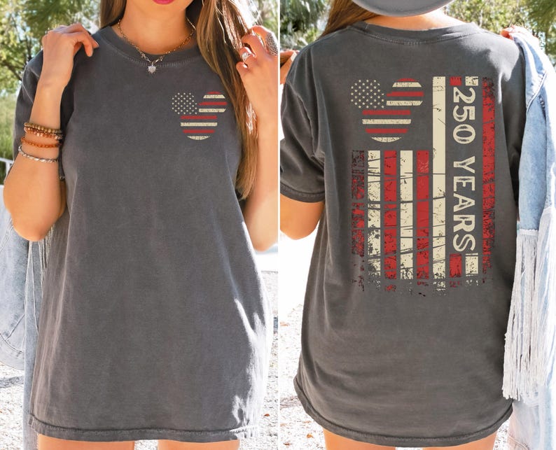 May include: Charcoal grey t-shirt featuring a distressed American flag design. The front has a Mickey Mouse head with stars and stripes. The back shows a larger flag design with "250 YEARS" text. A casual, patriotic tee.