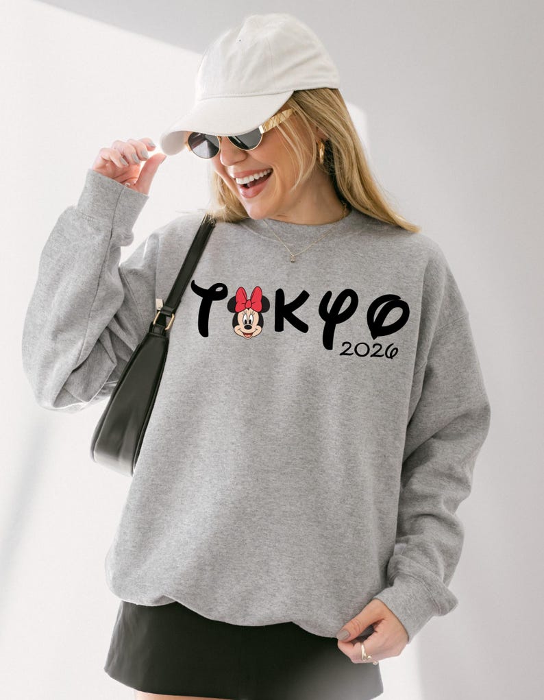 May include: Gray sweatshirt with the word "TOKYO" in black script, featuring a Minnie Mouse graphic and the year "2026". The sweatshirt is a crew neck style.