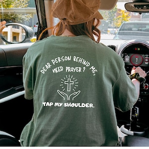 May include: A green t-shirt with the text "Dear person behind me, need prayer? Tap my shoulder." and a white cross graphic.
