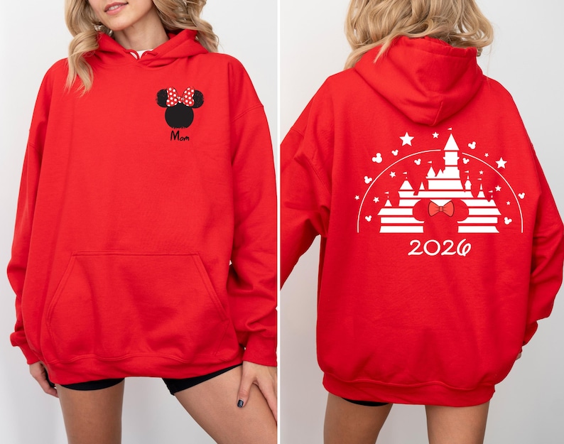 Puede incluir: Una sudadera con capucha roja con un bolsillo delantero y un dise&ntilde;o de Minnie Mouse. La parte delantera presenta una silueta negra de Minnie Mouse con un lazo de lunares rojos y blancos y la palabra "Mam&aacute;". La parte trasera muestra un dise&ntilde;o de castillo blanco con el a&ntilde;o "2026".