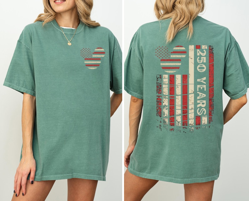 May include: A sage green t-shirt featuring a Mickey Mouse head design on the front and back. The design incorporates red and white stripes and stars, with the text "250 YEARS" on the back, in a vintage style.