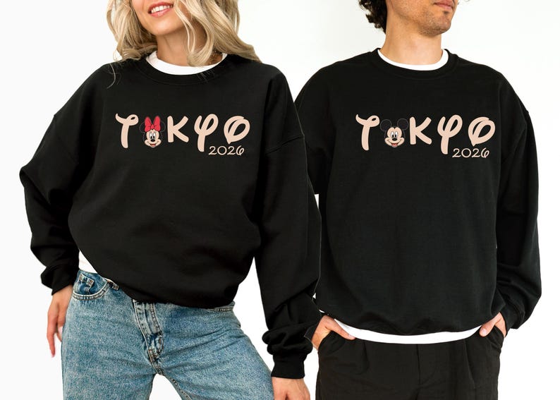 May include: Black sweatshirts with the word "TOKYO" in a stylized font, featuring Mickey and Minnie Mouse characters. The year "2026" is below the word. The sweatshirts have a crew neck and long sleeves.