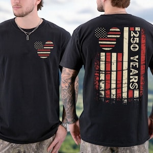 May include: Black t-shirt with a patriotic design. The front features a Mickey Mouse head in a US flag pattern. The back displays a larger flag design with the text "250 YEARS". A casual, comfortable garment.