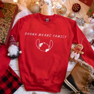 May include: A red sweatshirt featuring the text "OHANA MEANS FAMILY" and a white character outline. The image includes festive decorations such as a gift box, baubles, and a gingerbread man, perfect for the holiday season.