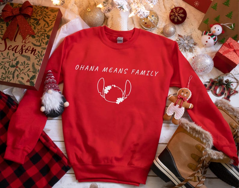 May include: A red sweatshirt featuring the text "OHANA MEANS FAMILY" and a white character outline. The image includes festive decorations such as a gift box, baubles, and a gingerbread man, perfect for the holiday season.