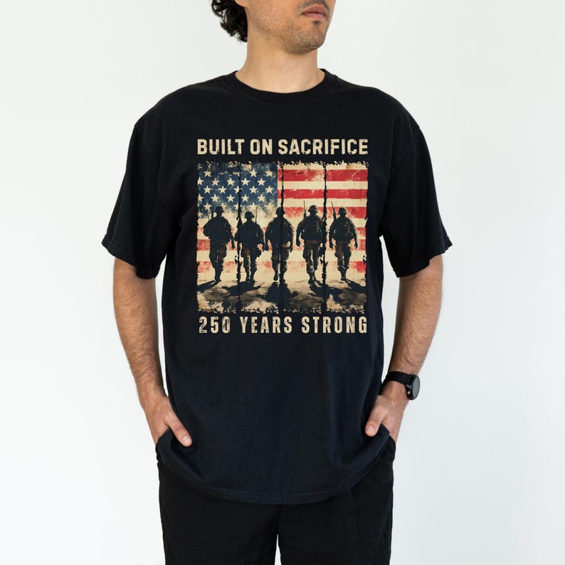 May include: Black t-shirt featuring an American flag design with soldiers and the text "BUILT ON SACRIFICE" and "250 YEARS STRONG." The graphic is distressed, giving a vintage look.