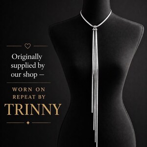 May include: A silver-toned necklace with a long, cascading fringe design. The necklace is displayed on a black mannequin against a black background. The text on the left side says "Originally supplied by our shop - WORN ON REPEAT BY TRINNY."