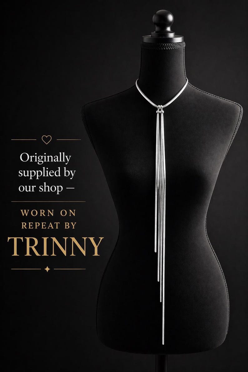 May include: A silver-toned necklace with a long, cascading fringe design. The necklace is displayed on a black mannequin against a black background. The text on the left side says "Originally supplied by our shop - WORN ON REPEAT BY TRINNY."