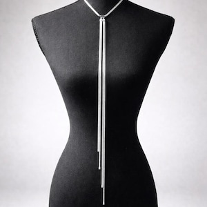 May include: A silver-toned lariat necklace displayed on a black mannequin. The necklace features a delicate chain that forms a Y-shape, with two long, slender strands hanging down. The text "LexieDjewels - Original supplier to Trinny Woodall" is visible.