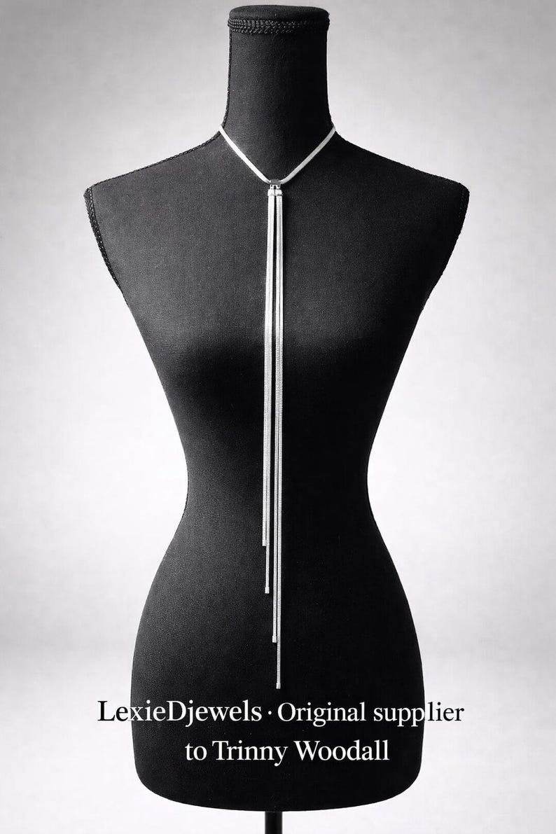 May include: A silver-toned lariat necklace displayed on a black mannequin. The necklace features a delicate chain that forms a Y-shape, with two long, slender strands hanging down. The text "LexieDjewels &bull; Original supplier to Trinny Woodall" is visible.