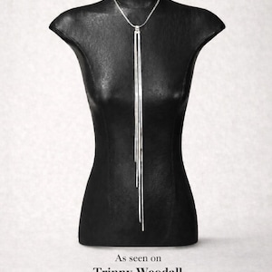 May include: A silver necklace with a vertical bar pendant, displayed on a black mannequin. The necklace has a delicate chain and three long, slender bars that hang down. The mannequin is on a white background.