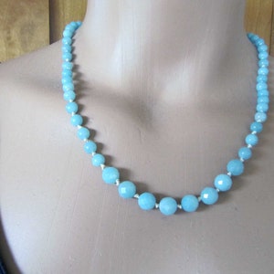 May include: A light blue gemstone necklace with faceted beads. The necklace is made of aquamarine beads and is strung on a white cord.