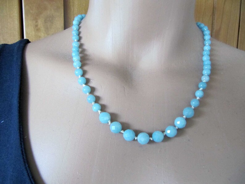 May include: A light blue gemstone necklace with faceted beads. The necklace is made of aquamarine beads and is strung on a white cord.