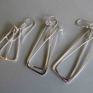 May include: Three pairs of silver earrings with geometric designs. The earrings are made of thin metal and have a simple, modern look.