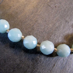 May include: A close-up of a light blue gemstone necklace with faceted beads. The beads are strung on a thin white cord.