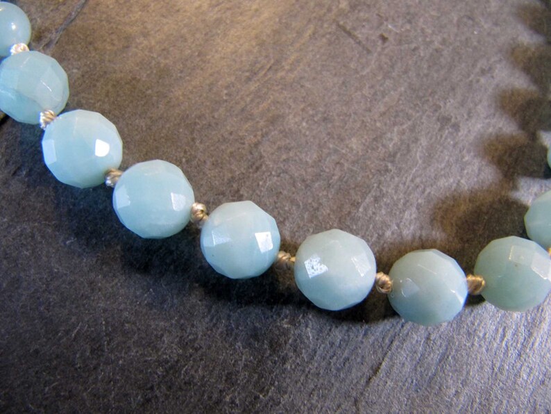 May include: A close-up of a light blue gemstone necklace with faceted beads. The beads are strung on a thin white cord.