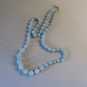 May include: A light blue gemstone necklace with silver beads. The necklace is made of round beads and is strung on a silver chain.