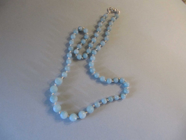May include: A light blue gemstone necklace with silver beads. The necklace is made of round beads and is strung on a silver chain.