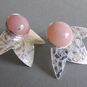 May include: A pair of silver earrings with pink opal stones set in a leaf-shaped design.