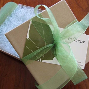 May include: A brown gift box with a green ribbon and a business card that reads "Albeen Frazer Designs". The box is filled with white tissue paper.
